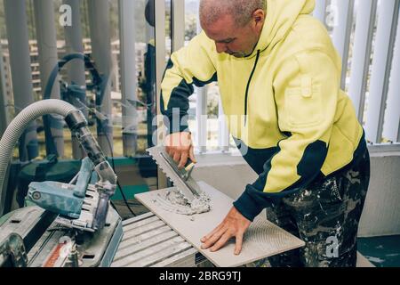 Professioneller Baumeister verschmiert Zementleim auf der Keramikfliesen mit einer Kelle. Konzept Renovierung Reparatur, Überholung, Auftragskachel. Stockfoto