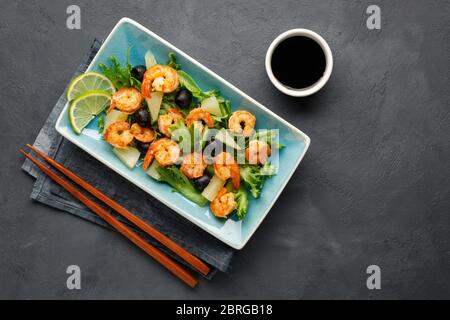 Salat mit Garnelen, Ananas und frischen Kräutern in einem blauen Teller auf schwarzem Hintergrund. Gesunde Ernährung. Draufsicht. Stockfoto