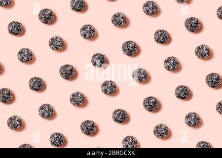 Gesunde rohe Energiebälle aus getrockneten Früchten und Nüssen mit Kokosnusssplittern, Leinsamen, Pistazien, Sesam. Muster auf rosa Hintergrund. Stockfoto