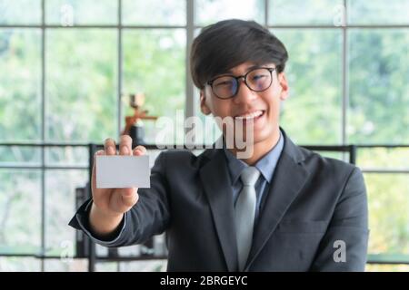 Junge asiatische Geschäftsmann trägt einen Anzug halten und zeigt Vorderseite Ansicht eine weiße leere Visitenkarte Mockup. Konzept der professionellen Stelle dich vor Stockfoto