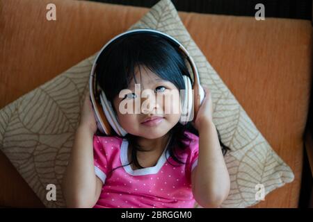 Happy Asian Mädchen lächelnd und genießt Musik in Kopfhörern auf dem Sofa Wohnzimmer hören Stockfoto