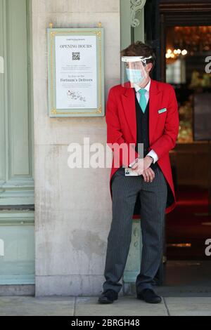 Ein uniformierter Türsteher trägt eine Maske und ein Visier vor dem Eingang des Kaufhauses Fortnum & Mason in Piccadilly, im Zentrum Londons, das seit heute zwei Food Halls für Kunden eröffnet hat, da die Beschränkungen für die Sperrung des Coronavirus gelockert werden. Stockfoto