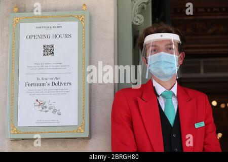 Ein uniformierter Türsteher trägt eine Maske und ein Visier vor dem Eingang des Kaufhauses Fortnum & Mason in Piccadilly, im Zentrum Londons, das seit heute zwei Food Halls für Kunden eröffnet hat, da die Beschränkungen für die Sperrung des Coronavirus gelockert werden. Stockfoto