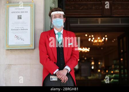 Ein uniformierter Türsteher trägt eine Maske und ein Visier vor dem Eingang des Kaufhauses Fortnum & Mason in Piccadilly, im Zentrum Londons, das seit heute zwei Food Halls für Kunden eröffnet hat, da die Beschränkungen für die Sperrung des Coronavirus gelockert werden. Stockfoto