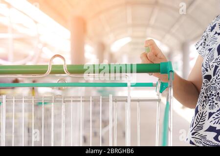 Frau tragen Maske mit Spritzen Alkohol antiseptische Desinfektionsmittel Spray Reinigung auf Warenkorb Trolley Griff Schutz während Coronavirus Pandemie C Stockfoto