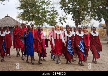 Maasai Dorf, Männer, Frauen, Touristen besuchen, Safari, Stammeskleidung, rot, gemeinsam zu Fuß, Reetdach, Reiseerlebnis, Tansania; Afrika Stockfoto