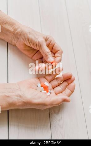 Ältere Hände mit Pillen und Drogen auf einem hellen Tisch, Holzhintergrund. Faltige Hände einer alten Frau, die bunte Tabletten hält. Schmerzhaftes Alter. Gesundheitsfahrzeug Stockfoto