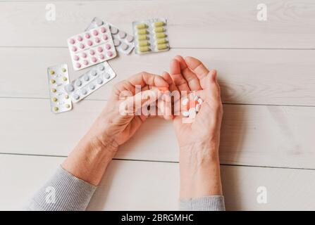 Ältere Hände mit Pillen und Drogen auf einem hellen Tisch, Holzhintergrund. Faltige Hände einer alten Frau, die bunte Tabletten hält. Schmerzhaftes Alter. Gesundheitsfahrzeug Stockfoto