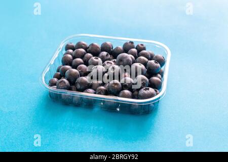 Frische Heidelbeere aus dem Wald in Plastikbehälter auf blauem Hintergrund Stockfoto