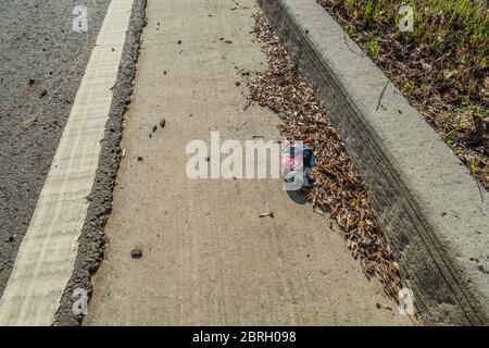 Eine zerknitterte Coca-Cola kann auf der Straße entlang der Bordsteinkante mit anderen Trümmern, die die Umwelt an einem hellen sonnigen Tag verschmutzen weggeworfen Stockfoto