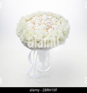 Weißer Strauß von Marshmallows und Pralinen, eingerahmt von weißen Blumen, steht in einer Vase auf weißem Hintergrund. Stockfoto