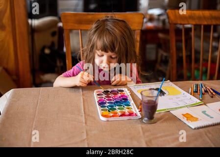 Ein 5-jähriges Mädchen malt mit einer Vielzahl von Aquarellfarben. Stockfoto