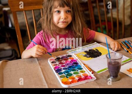 Ein 5-jähriges Mädchen malt mit einer Vielzahl von Aquarellfarben. Stockfoto