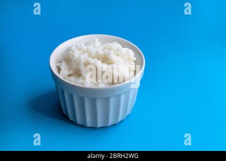 Leckerer Reisbrei in einer weißen Schüssel auf blauem Hintergrund. Richtige gesunde Ernährung Konzept. Stockfoto