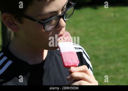 Kind genießt einen FAB Eis Lully an einem sonnigen Tag draußen in einem britischen Garten Stockfoto