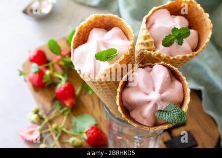 Hausgemachte Bio-Erdbeer-Eiscreme. Erdbeere von Eis in Waffelzapfen auf einem hellen Stein oder Schiefer Tisch. Draufsicht flach legen Hintergrund. Stockfoto
