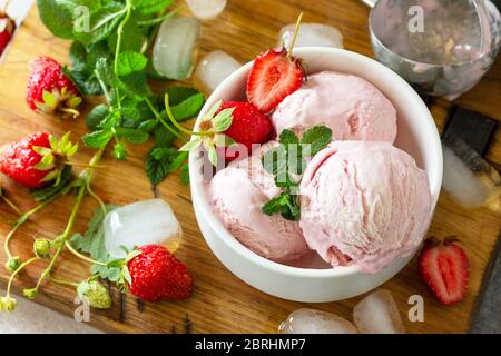 Hausgemachte Bio-Erdbeer-Eiscreme. Erdbeer Eiskugeln mit Minzblättern auf einem hellen Stein- oder Schiefertisch. Stockfoto