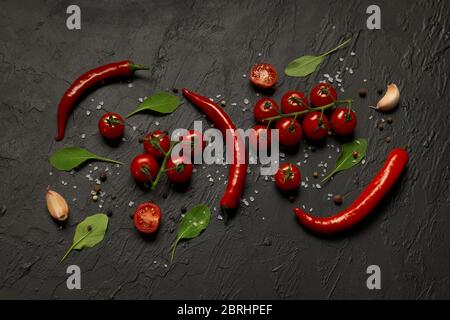 Scharfe Chilischoten, Kirschtomaten, Knoblauch, Rucola-Blätter und Gewürze auf schwarzem Hintergrund. Stockfoto