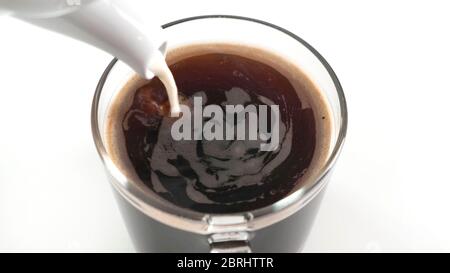 Geben Sie Milch zu einer Tasse Kaffee auf dem Küchentisch. Nahaufnahme. Stockfoto