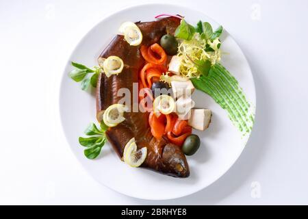 Fischgericht mit Gemüse, Scheiben Käse, Zitrone, Oliven und Kräutern auf einem weißen Teller auf hellem Hintergrund Stockfoto