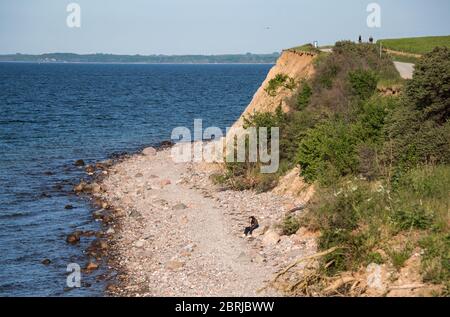 21. Mai 2020, Schleswig-Holstein, Lübeck-Travemünde: Ein Paar sitzt am Brodtener Steilufer am Ostseestrand, zwei Radfahrer sind an der Steilküste unterwegs. Foto: Daniel Bockwoldt/dpa Stockfoto