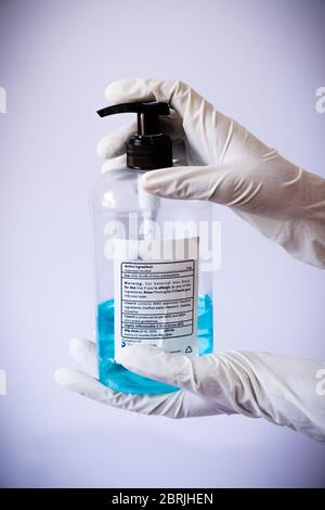 Desinfektionsflasche mit beiden Händen mit medizinischen Latexhandschuhen präsentieren Stockfoto