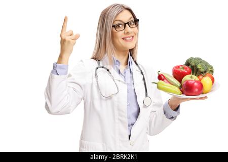 Ärztin hält einen Teller mit frischem Obst und Gemüse und zeigt isoliert auf weißem Hintergrund Stockfoto