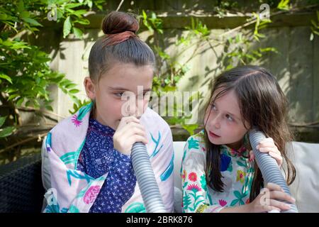 Zwei junge Mädchen hören zu und reden Schlauchleitung hinunter Stockfoto