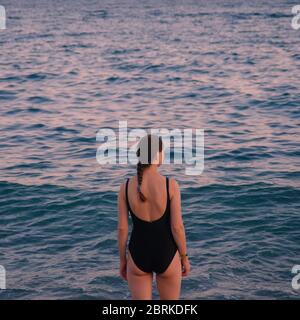 Mädchen in einem schwarzen Badeanzug mit dem Rücken zum Meer Stockfoto