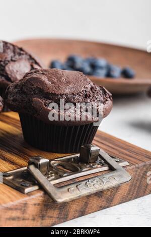 Leckere hausgemachte Schokoladenmuffins auf rustikalem Holzbrett, frische Sommerbluebeeren in Keramikplatte Stockfoto