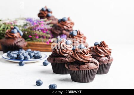 Leckere hausgemachte Schokolade Cupcakes auf rustikalem Holzbrett, frische Sommer Wildblume und Heidelbeeren in Keramikplatte Stockfoto