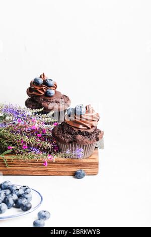 Leckere hausgemachte Schokolade Cupcakes auf rustikalem Holzbrett, frische Sommer Wildblume und Heidelbeeren in Keramikplatte Stockfoto