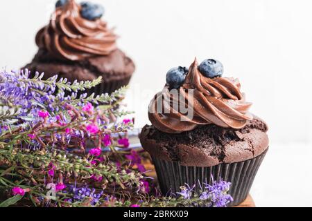 Leckere hausgemachte Schokolade Cupcakes auf rustikalem Holzbrett, frische Sommer Wildblume und Heidelbeeren in Keramikplatte Stockfoto