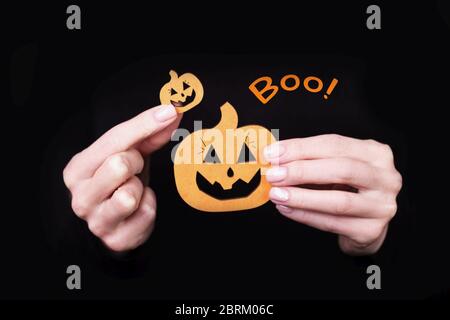 Weibliche Hände halten lustige kleine Kürbisse auf schwarzem Hintergrund. Halloween Karte mit Boo Inschrift Stockfoto