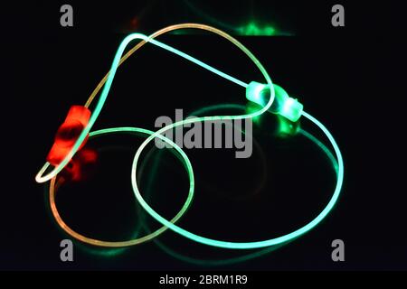 Draht mit grünem und rotem Licht, ein Lichtleiterkabel mit unterschiedlicher Lichtübertragung, Lichtspektrum und Lichteffekten in einem chaotischen Zustand. Stockfoto