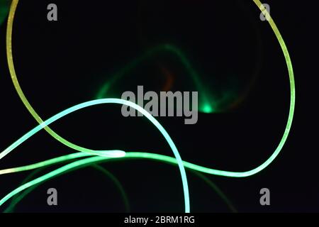 Draht mit grünem und rotem Licht, ein Lichtleiterkabel mit unterschiedlicher Lichtübertragung, Lichtspektrum und Lichteffekten in einem chaotischen Zustand. Stockfoto