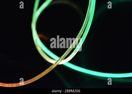 Draht mit grünem und rotem Licht, ein Lichtleiterkabel mit unterschiedlicher Lichtübertragung, Lichtspektrum und Lichteffekten in einem chaotischen Zustand. Stockfoto