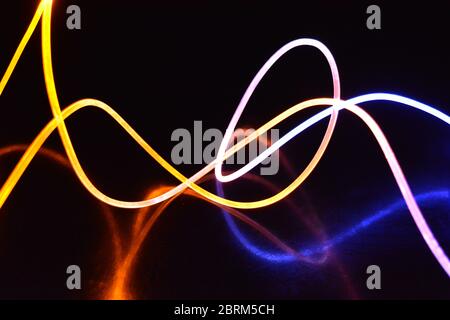 Gelbes und blaues Lichtkabel, ein Lichtleiterkabel mit unterschiedlicher Lichtdurchlässigkeit, unterschiedlichem Lichtspektrum und Lichteffekten, das sich in einem chaotischen Zustand befindet. Stockfoto