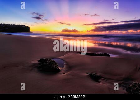 Dunkle Szenerie Sonnenaufgang an den Stränden von Sydney Northern um glatte Sand- und Sandsteinfelsen mit Blick auf den Osten und den hellen Meereshorizont. Stockfoto