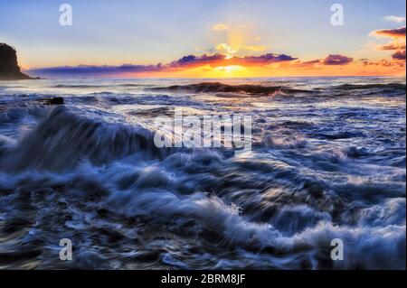 Bei spektakulärem Sonnenaufgang fliesst eine schnelle Welle des Pazifischen Ozeans über Felsen am Northern Beach in Sydney. Stockfoto