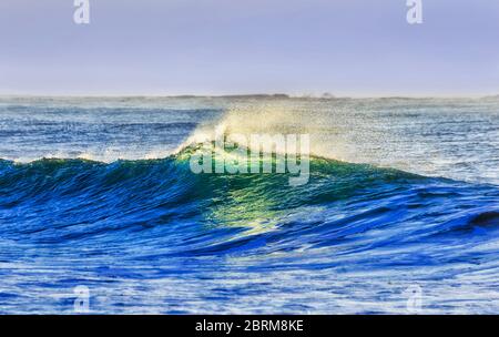 Steigende Welle rollt zum Bungan Beach von Sydney Northern Beaches bei Sonnenaufgang mit farbenfrohen Reflexen von der Oberfläche. Stockfoto