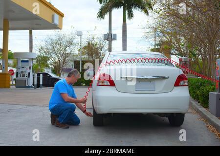 Mann füllt Autoreifen mit Luft an einer Tankstelle mit einer münzbetriebenen Kompressorpumpe, um den Druck auf die sichere Betriebsmenge zu bringen. Stockfoto