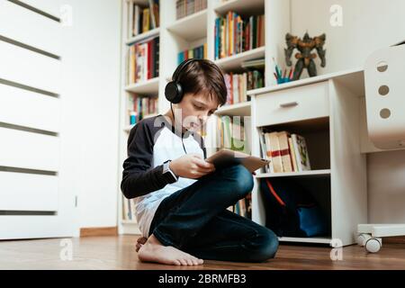 Knienden Jungen lernen auf digitalen Tablet zu Hause. Junger Student macht seine Hausaufgaben auf eigene Faust. Stockfoto