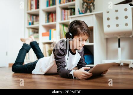 Junge Studentin mit Kopfhörern auf dem Boden liegend studieren zu Hause arbeiten mit digitalen Tablet. Junge entspannen und online lernen auf digitalen Tablet. Stockfoto