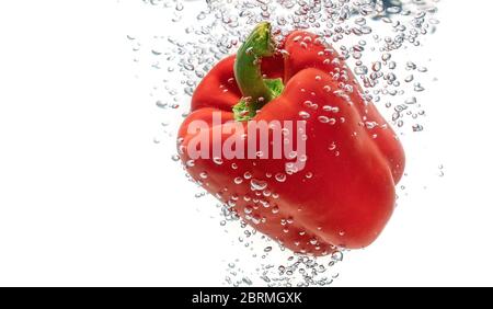 Saftig rot ökologische, Pfeffer fällt in sauberes Wasser erzeugt Blasen. Isoliert auf weißem Hintergrund. Stockfoto