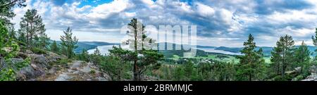 Sehr breites Panorama über wilde skandinavische Berge mit Kiefernwald, das Dorf und zwei Meeresbuchten, Sommertag mit schweren dramatischen Wolken, Norden Stockfoto