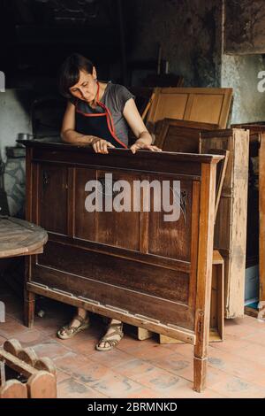 Weibliche Restauratorin, die mit alten Holzmöbeln in der Werkstatt arbeitet Stockfoto