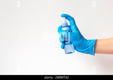 Weibliche Hand in blauen Schutzhandschuh hält Kunststoffflasche mit Desinfektor. Weißer Hintergrund, Kopierbereich. Gesundheits- und Hygienekonzept. Stockfoto