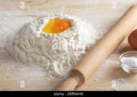 Der Prozess der Herstellung von Teig für hausgemachte köstliche traditionelle italienische Ravioli, Knödel mit Fleisch. Zerbrochenes rohes Ei in Mehl und Nudelholz auf einem Holz Stockfoto