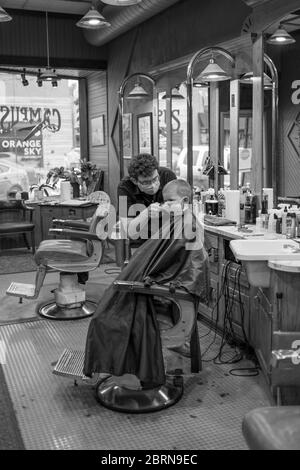 Manhattan, Kansas, USA. Mai 2020. DYLAN ROBERTS, Mitte, schneidet CALDER WEDDLE'S, 4, Haare am Mittwoch. Der Campus Barbershop in Aggieville, Kansas ältestem Einkaufsviertel, ist seit März 17 geschlossen und hat zwei Tage geöffnet. Mai 18 war der erste Tag der Phase 1.5 des Plans, Kansas Wirtschaft wieder zu öffnen. Kredit: Luke Townsend/ZUMA Wire/Alamy Live News Stockfoto